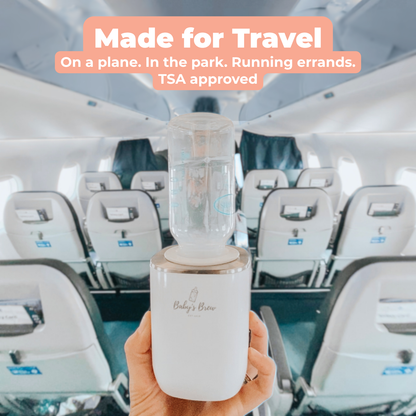 Hand holding a Baby's Brew portable bottle warmer with an attached baby bottle inside an airplane cabin by Mama's Dream