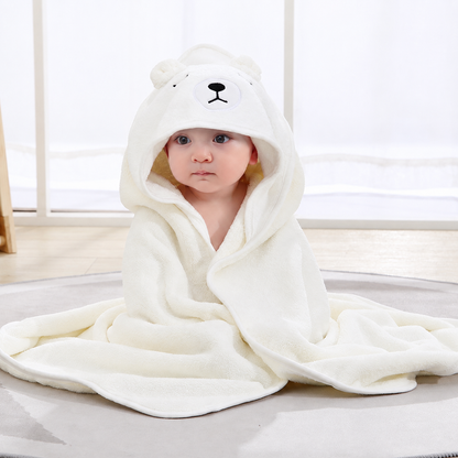 Baby sitting indoors wrapped in a soft cream hooded bath towel with an embroidered bear face by Mama's Dream