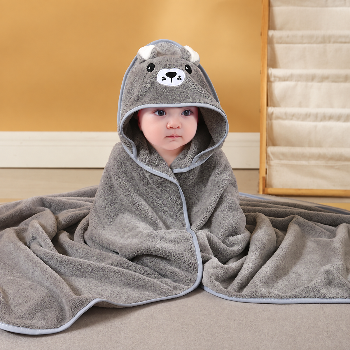 Baby wrapped in a soft gray hooded bath towel with an embroidered bear design by Mama's Dream