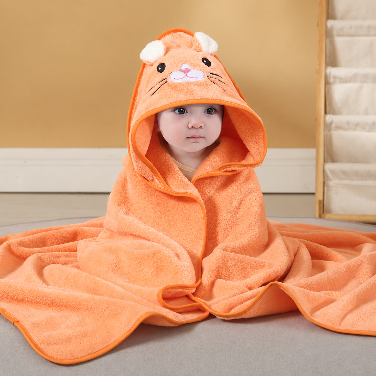 Baby wrapped in a soft orange hooded bath towel with an embroidered cat design by Mama's Dream